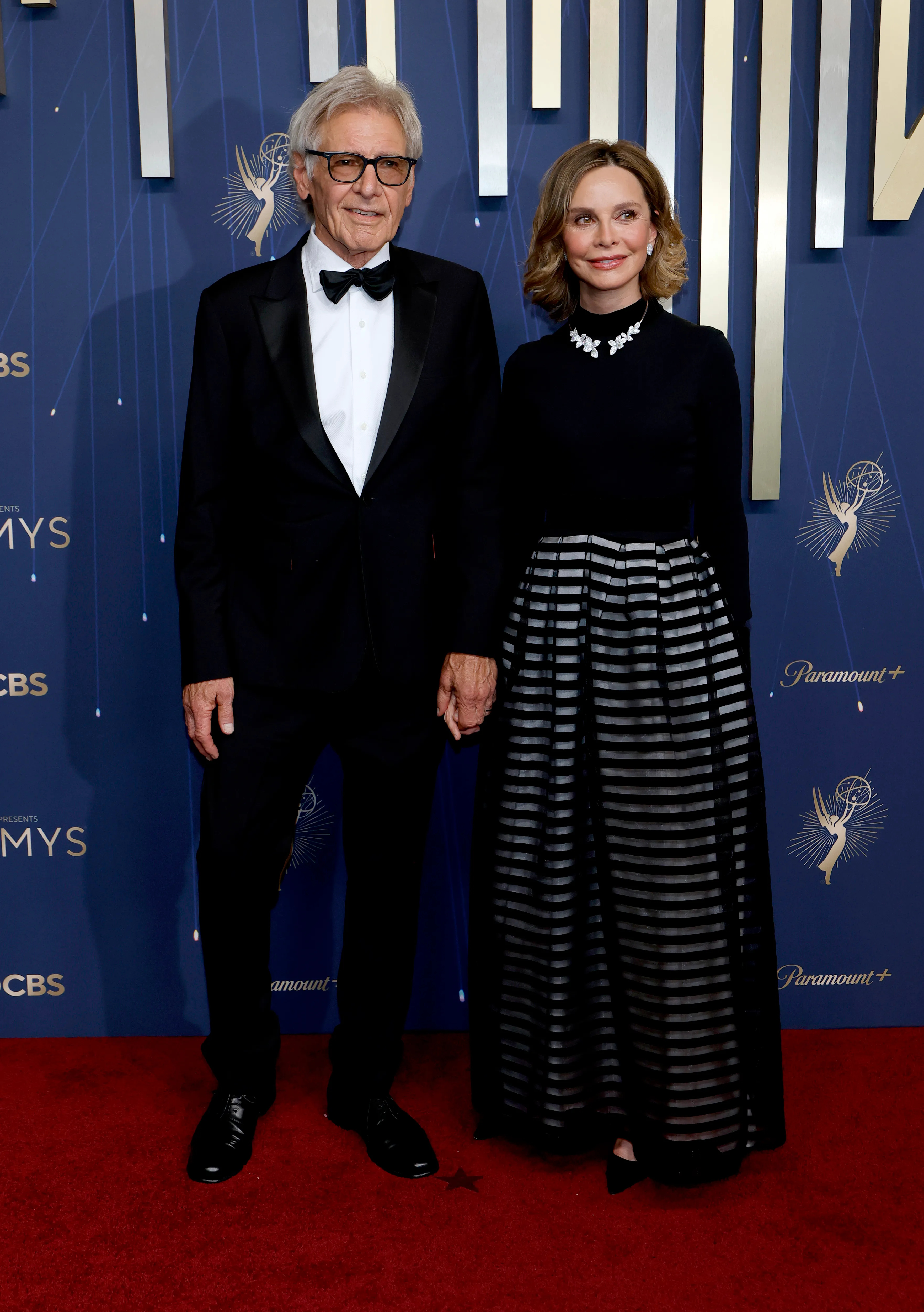 Harrison Ford in a tuxedo and Calista Flockhart in a black dress with a striped skirt attend the 77th Primetime Emmy Awards.