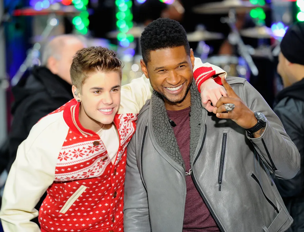 Justin Bieber and Usher smiling and posing together on stage.