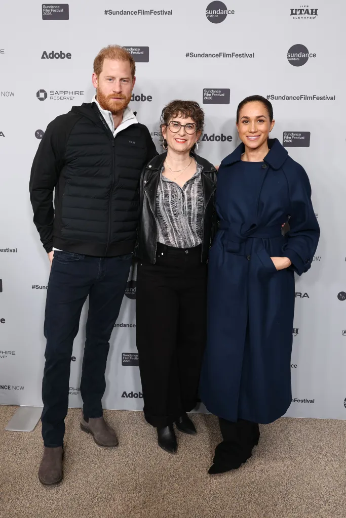 Prince Harry, in a black sweater, white shirt and black pants, Alysa Nahmias, in a grey striped shirt, black leather jacket and black pants, and Meghan Markle, in a navy blue coat and blue top and black pants, standing together at the 