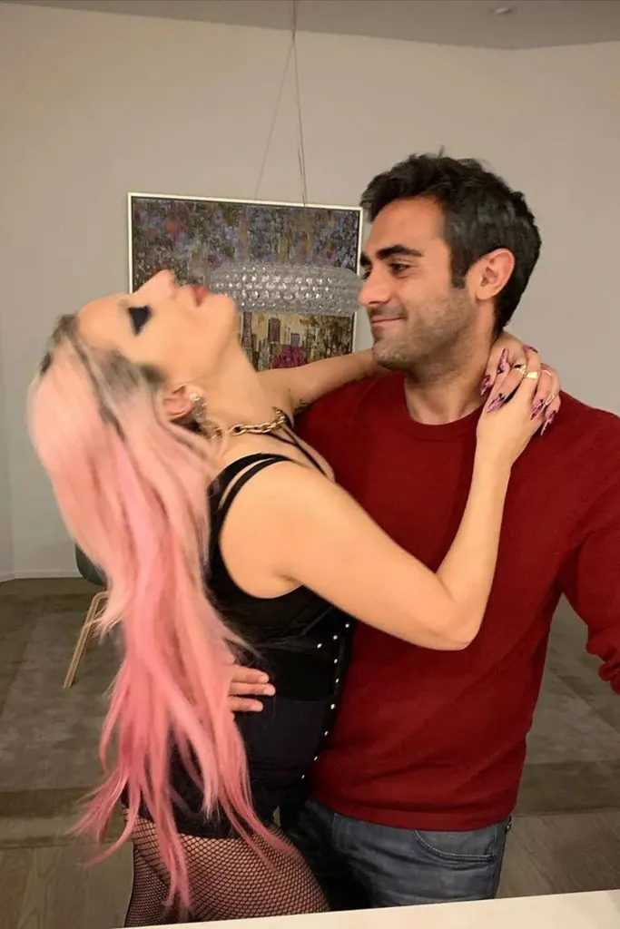 Lady Gaga in a black top and fishnets, with pink hair, embracing Michael Polansky in a red shirt and jeans.