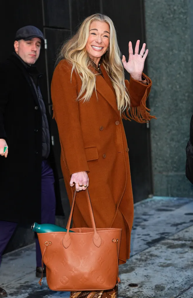 LeAnn Rimes waves, wearing a brown coat and holding a Louis Vuitton bag.