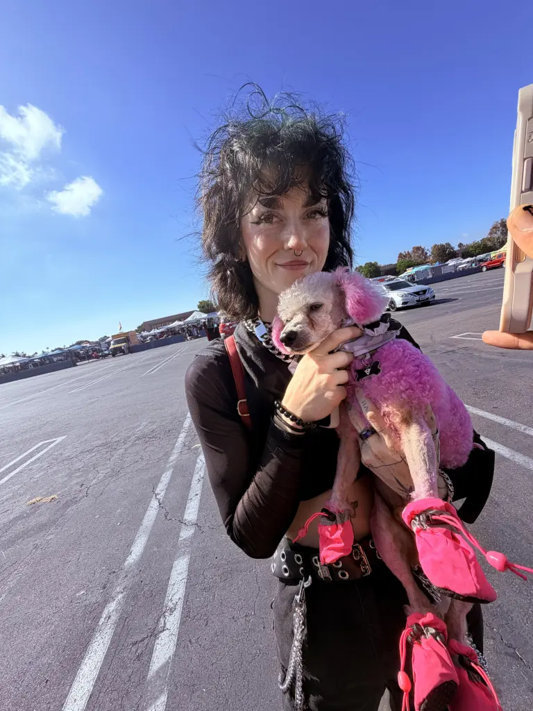 Lexi Bowman holding her dog, which has pink fur and pink booties, in a parking lot.