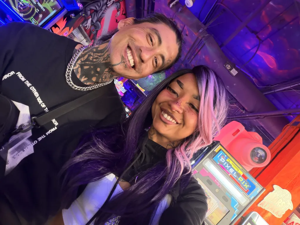 Frank and Tatyana smiling at the camera in a brightly lit room with arcade games and a 
