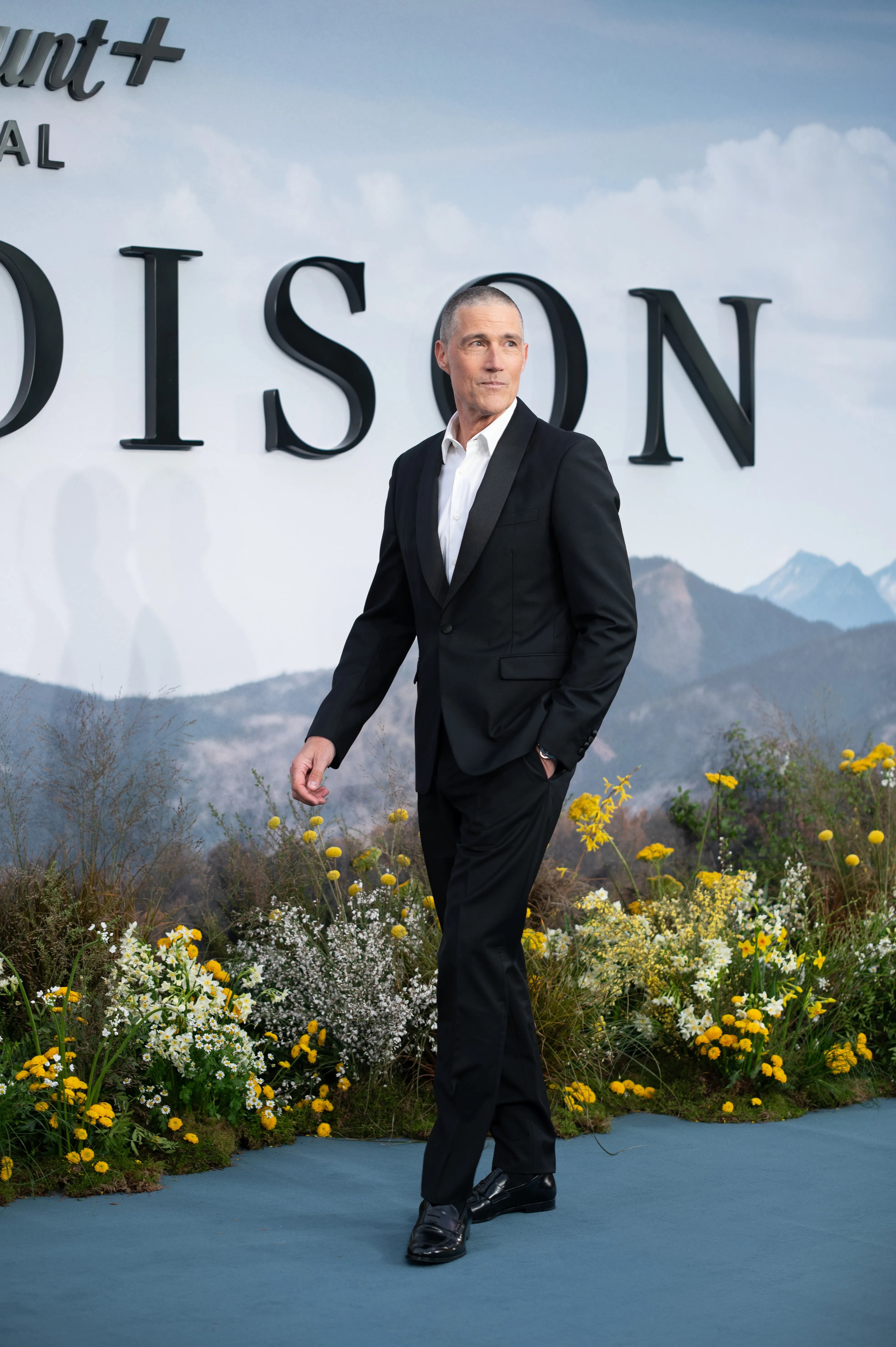 Matthew Fox in a black tuxedo on a red carpet with flowers at 