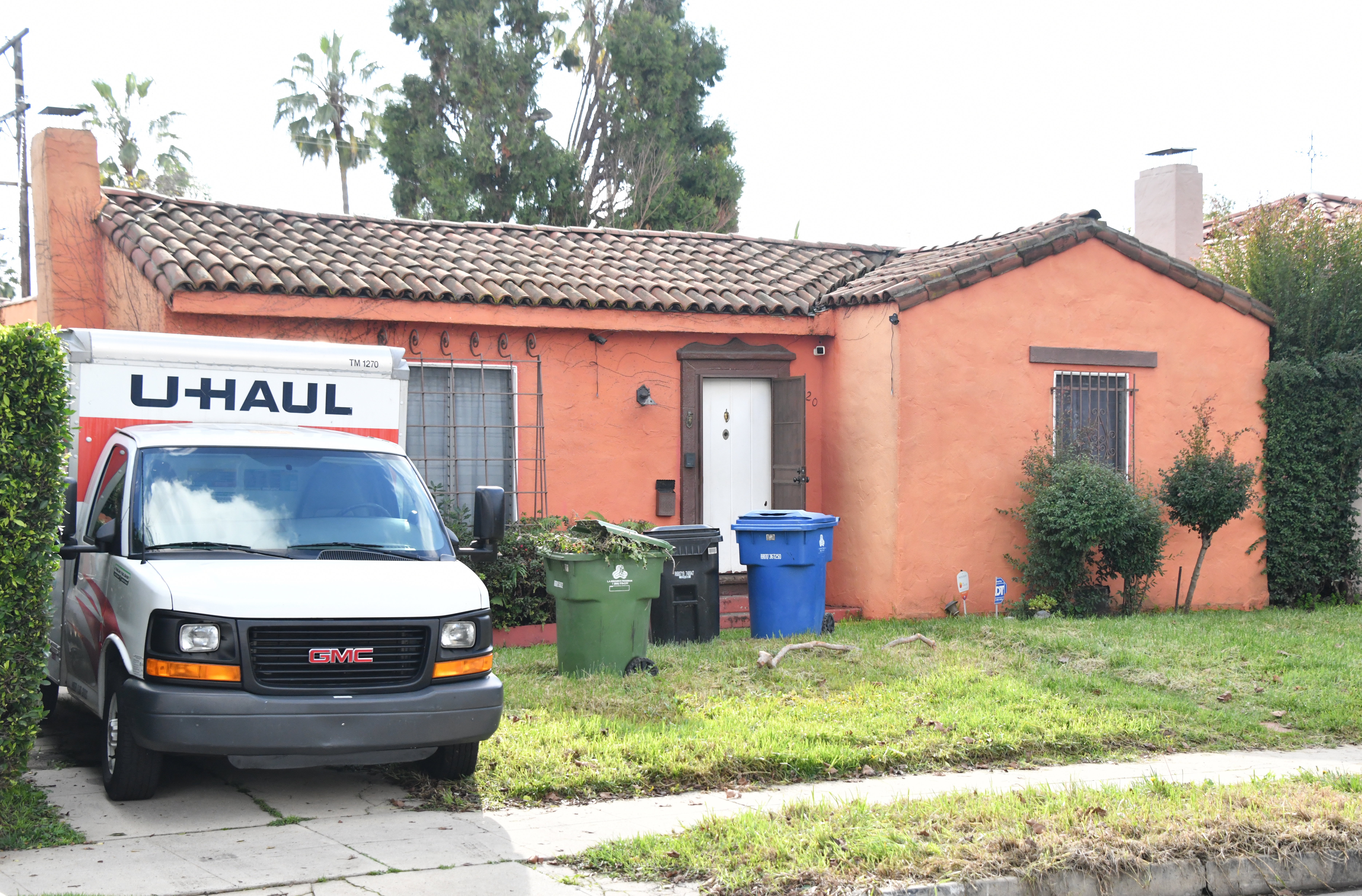 A white U-Haul truck parked in the driveway of an orange stucco house.