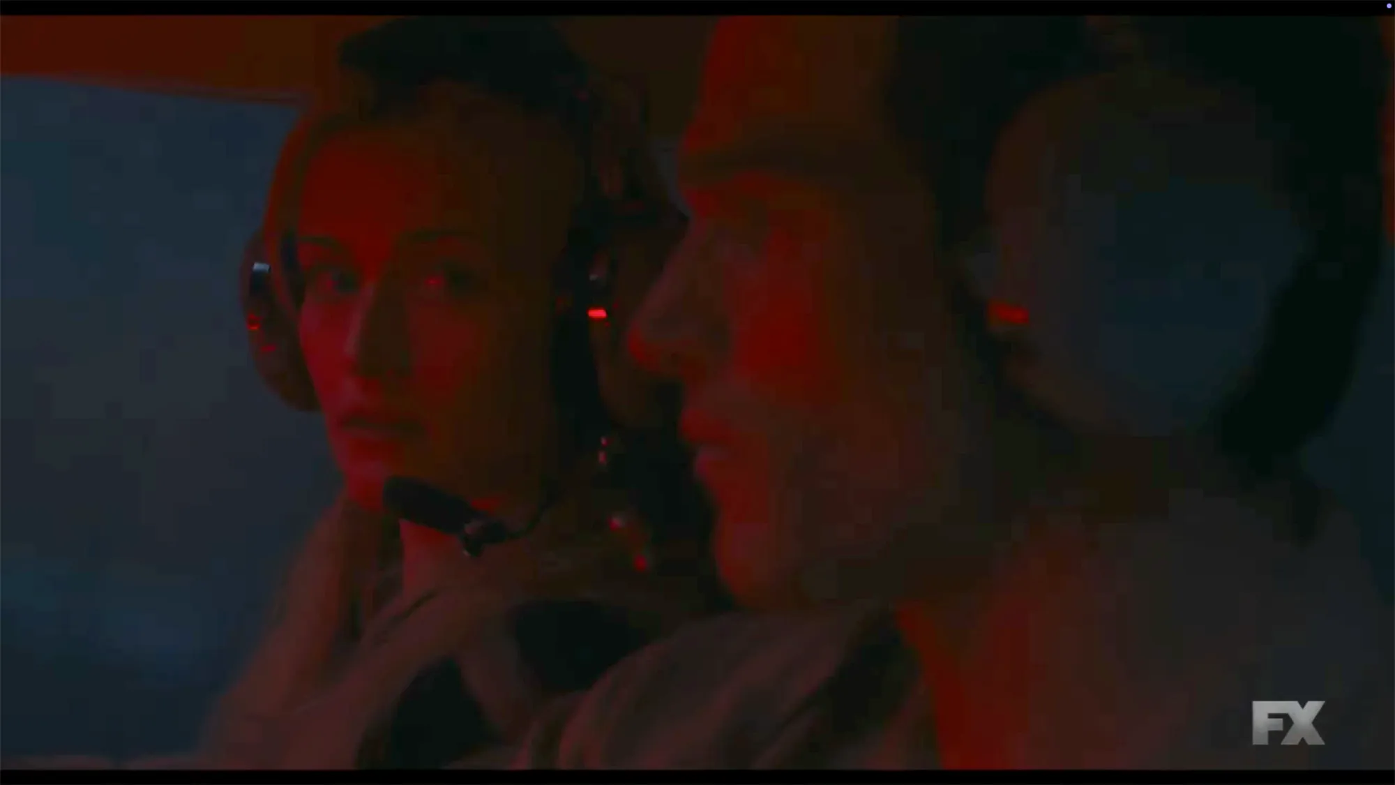 A woman and man wearing headsets, bathed in red light.