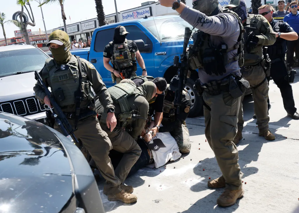 US Border Patrol agents arresting a man on the ground, surrounded by other agents and bystanders.