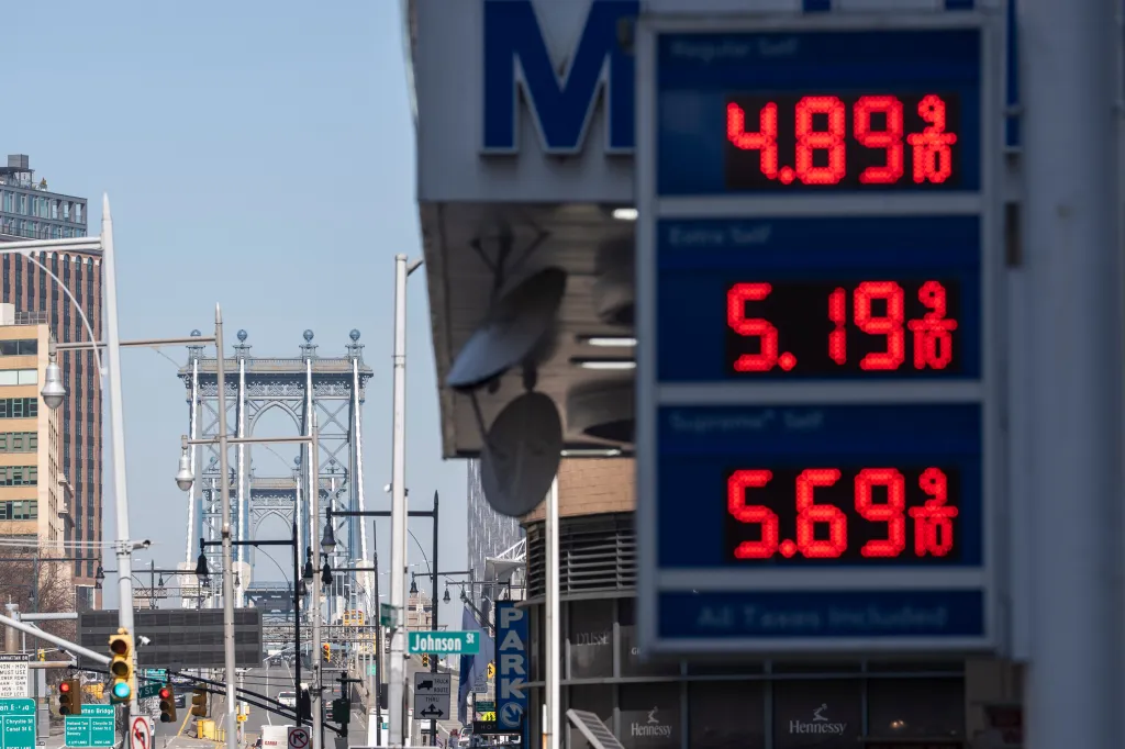 A gas station sign in Brooklyn, New York, shows regular gas at $4.89, mid-grade at $5.19, and premium at $5.69, with the Manhattan Bridge visible in the background.