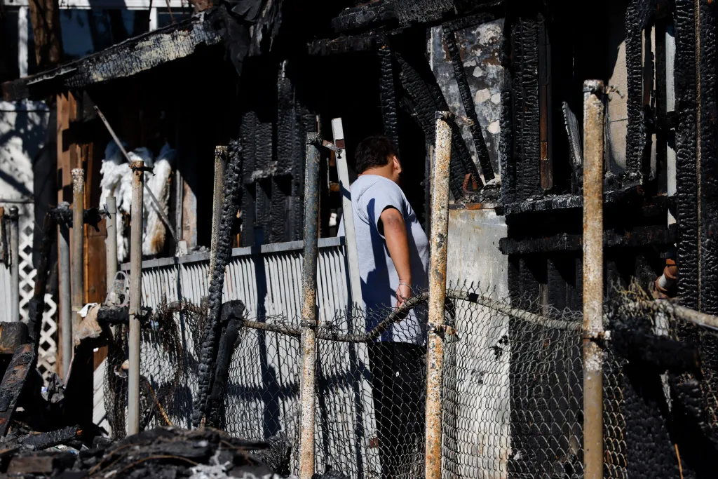 Jonathan Galicia walks through the burnt remains of his home after it caught fire from squatters in Larchmont.