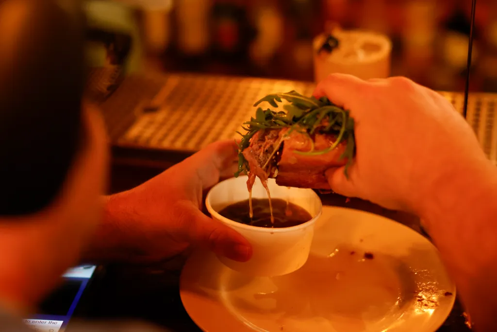 A French dip sandwich is dipped into a cup of au jus.