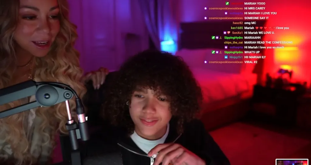 Mariah Carey surprising her son on a Twitch livestream as he sits in front of a monitor displaying chat messages.