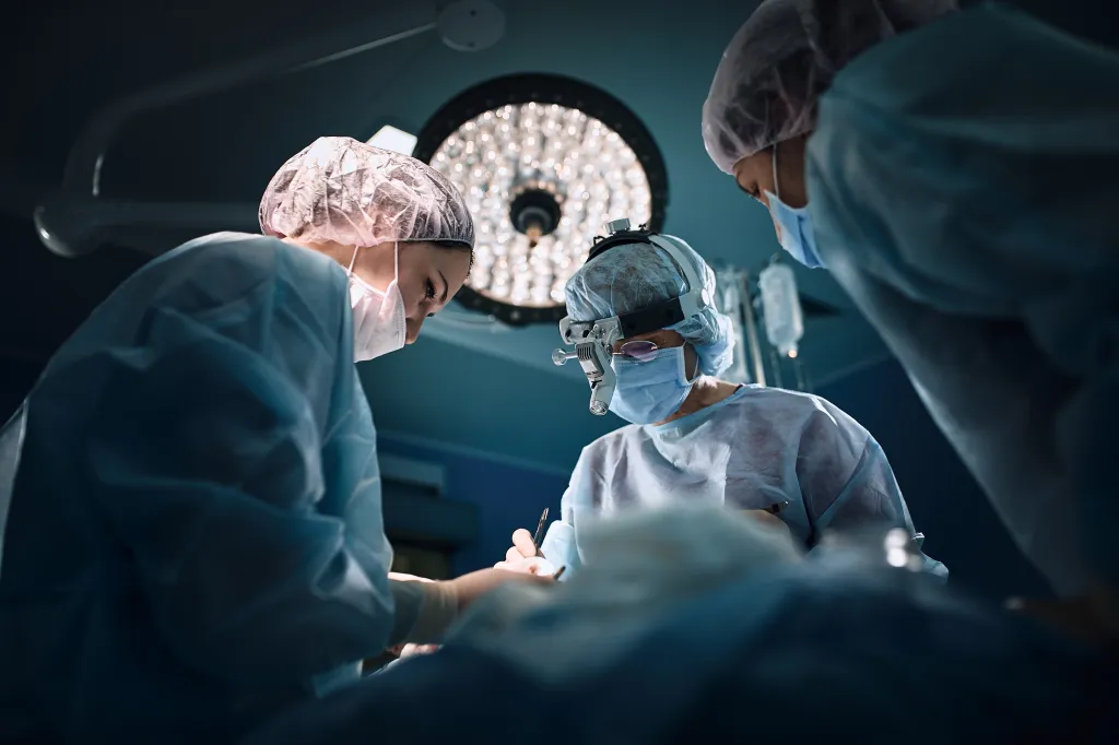 A medical team performing surgery in a dark operating room under bright surgical lights.