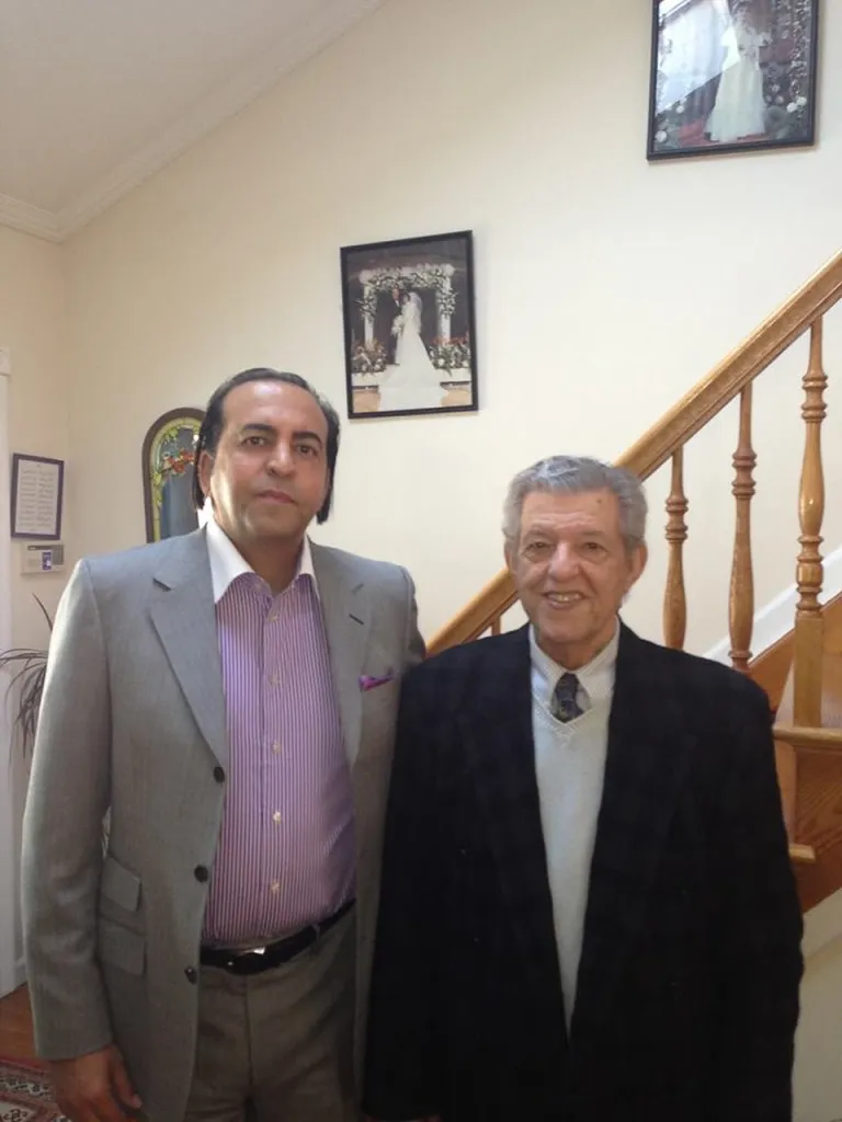 Kambiz Merabi and a man in a black jacket stand in an entryway with a wooden staircase.