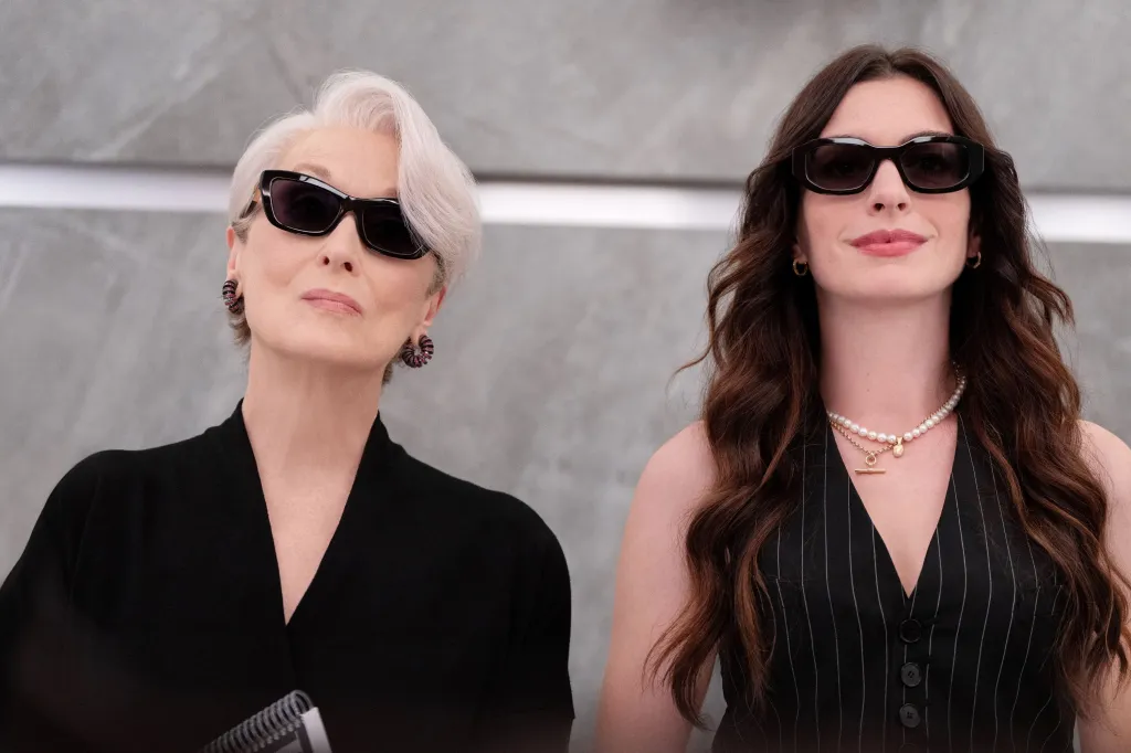 Meryl Streep, in a black jacket and sunglasses, and Anne Hathaway, in a black pinstriped waistcoat and sunglasses. 