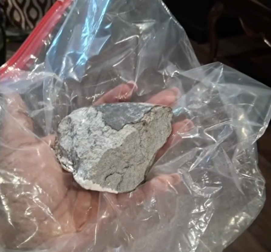 A person holding a gray meteor in a clear plastic bag.