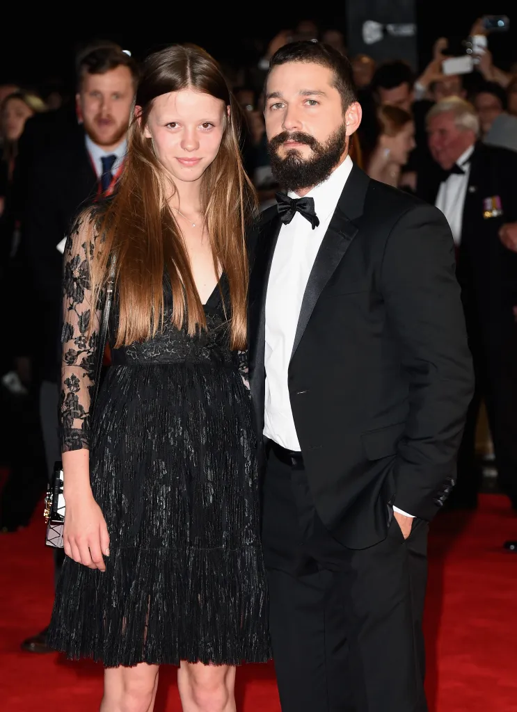 Mia Goth, in a black dress, and Shia LaBeouf, in a black tuxedo suit, on a red carpet.
