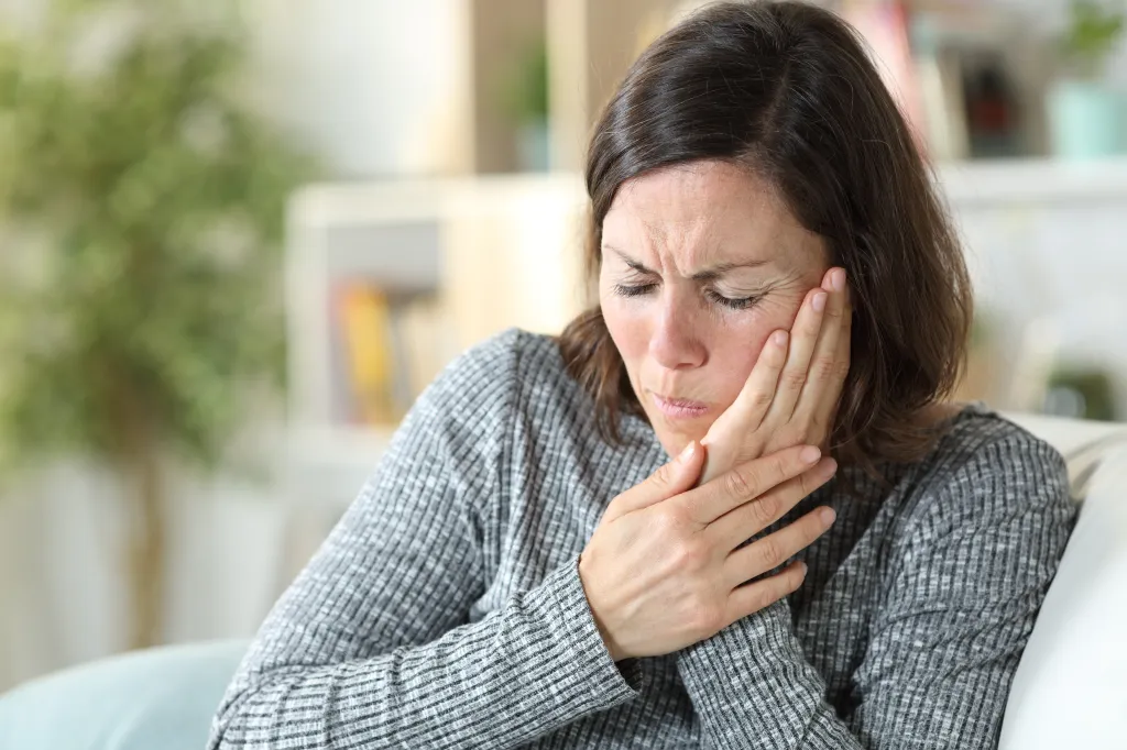 A middle-aged woman suffering from a toothache at home.