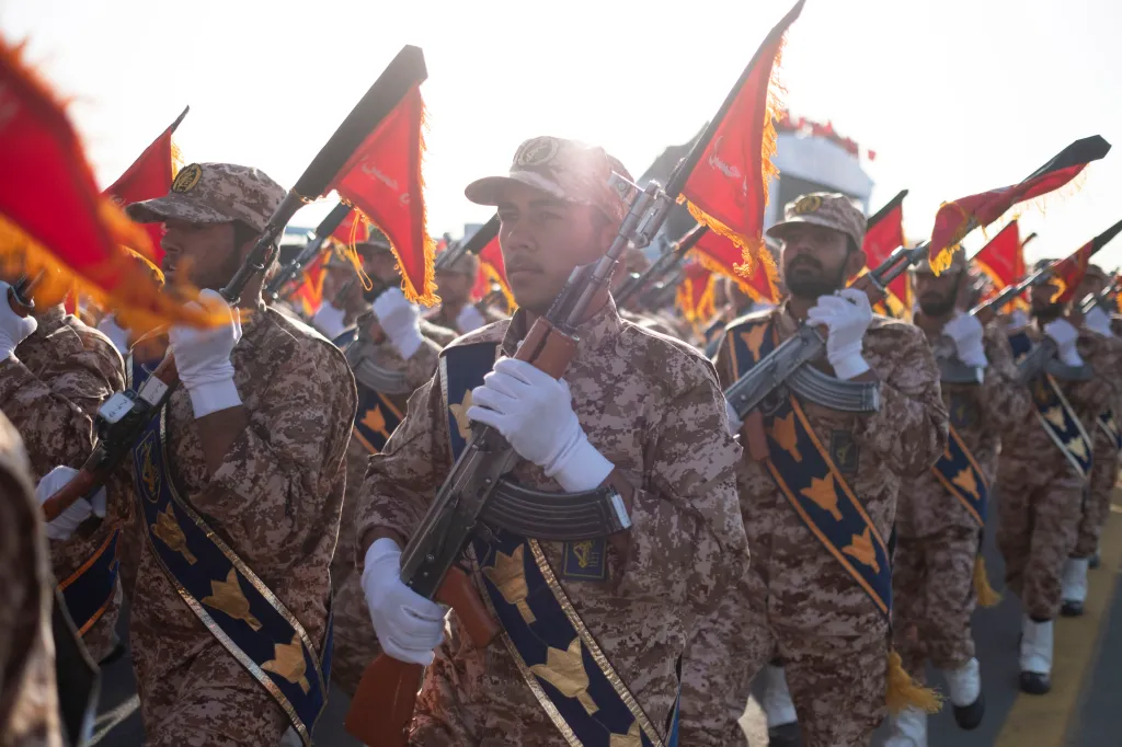 IRGC military personnel marching in a parade, holding rifles and red flags.