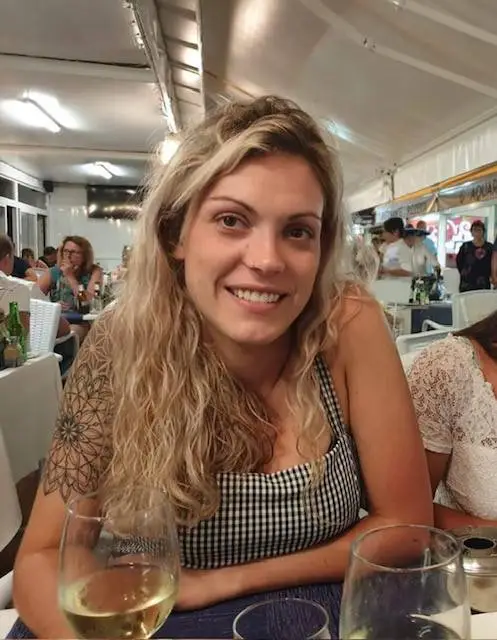 Missing backpacker Celine Cremer smiling while sitting at a table with a glass of white wine.