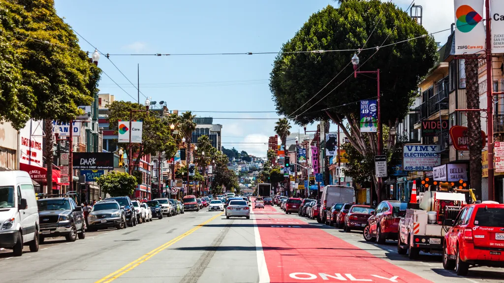 A street view of Mission District in San Francisco with cars parked along the curb and driving down the street.