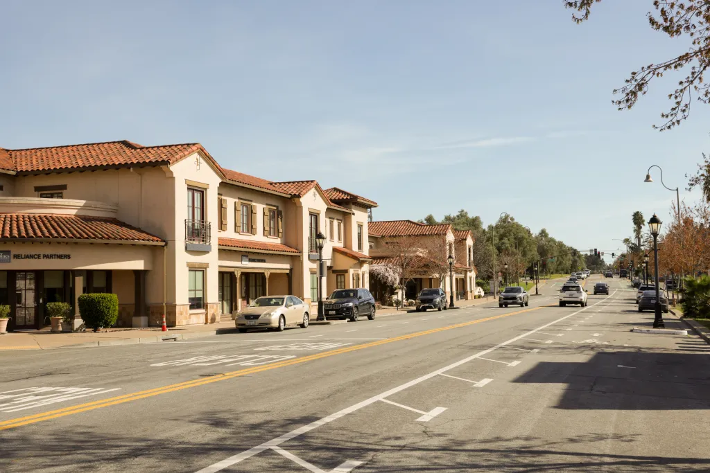 A street view of Mission San Jose neighborhood in Fremont, CA, with Spanish colonial revival buildings and cars parked alongside the road.