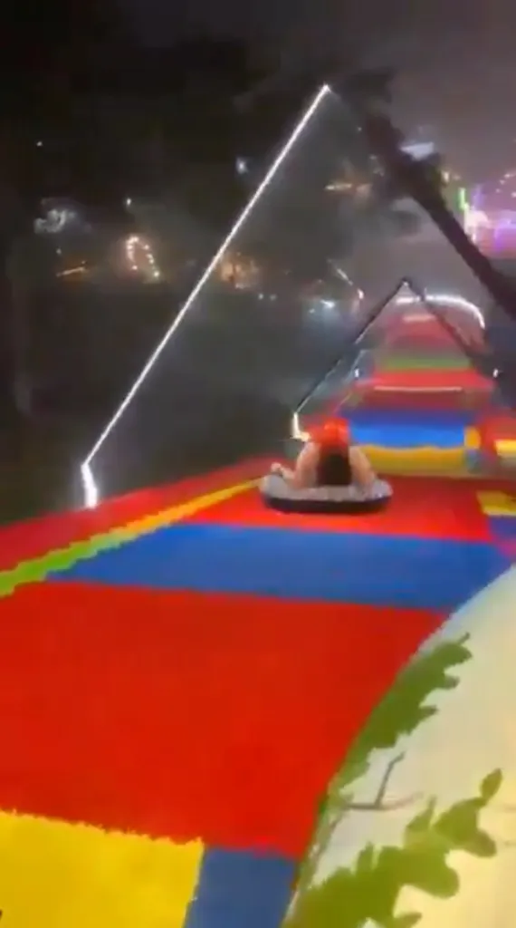 A person in an inner tube on a colorful amusement park slide at night.