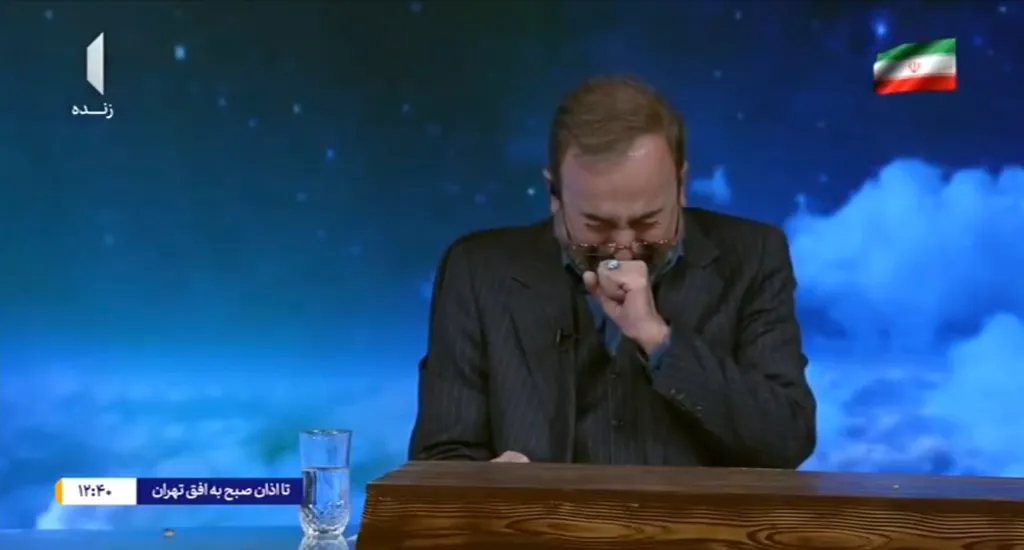 A tearful male TV host covering his mouth with his fist, with the Iranian flag shown in the upper right corner.