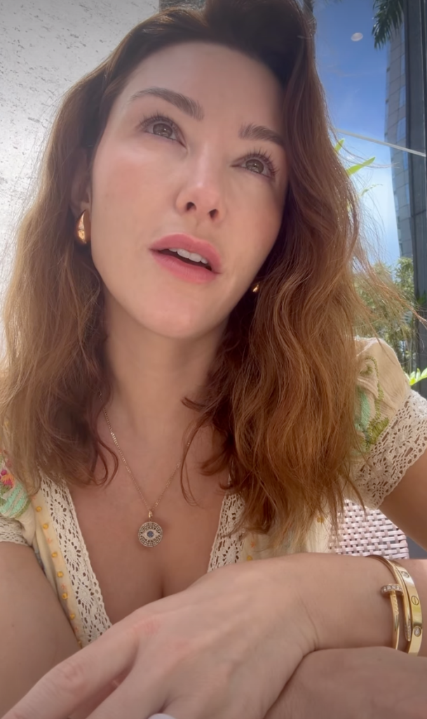 Close-up of a woman looking upwards, wearing a lacy top, a necklace, and bracelets.