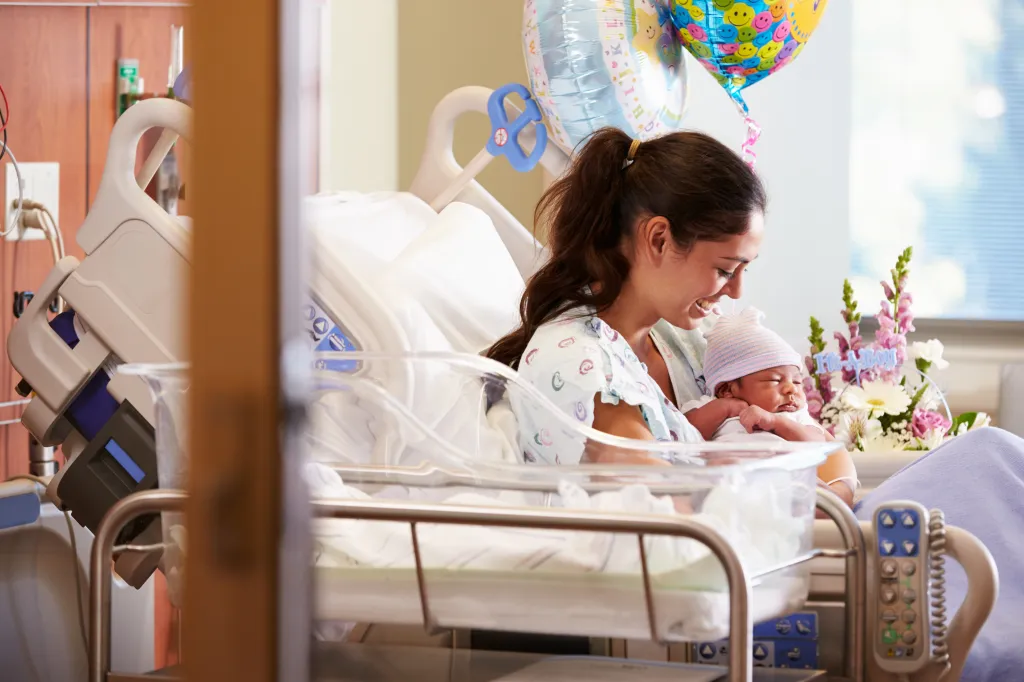 A mother smiling while holding her newborn baby in a hospital bed.