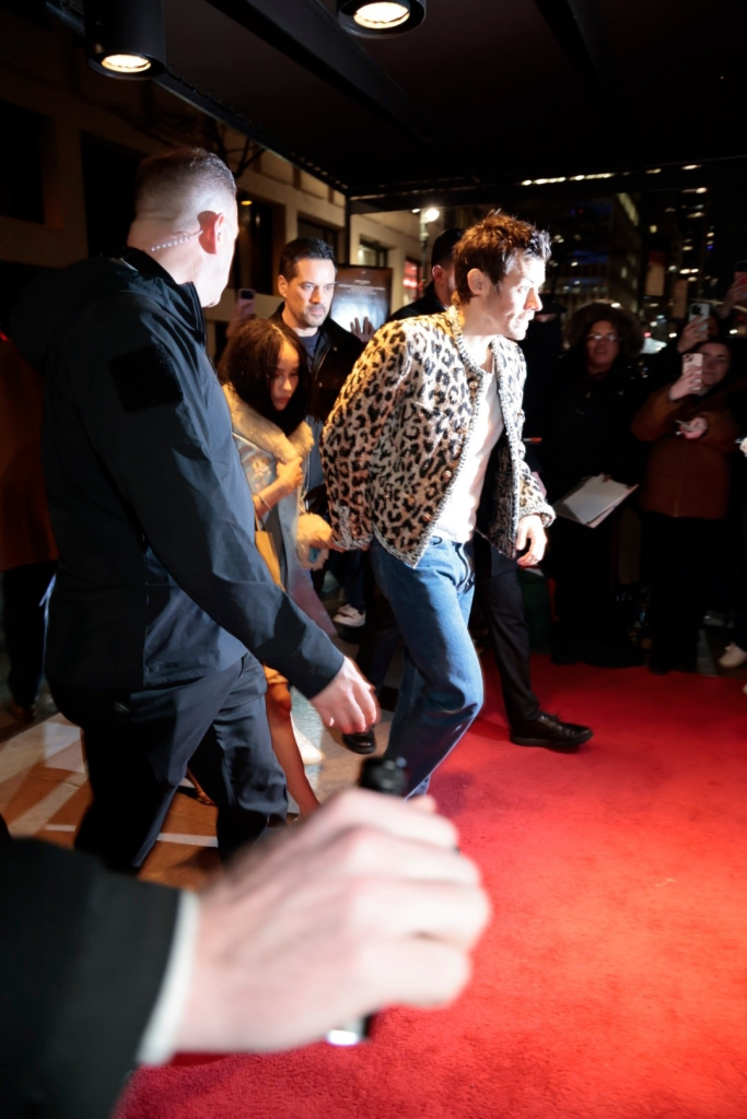 Harry Styles in a leopard print jacket walks on a red carpet at an SNL afterparty.