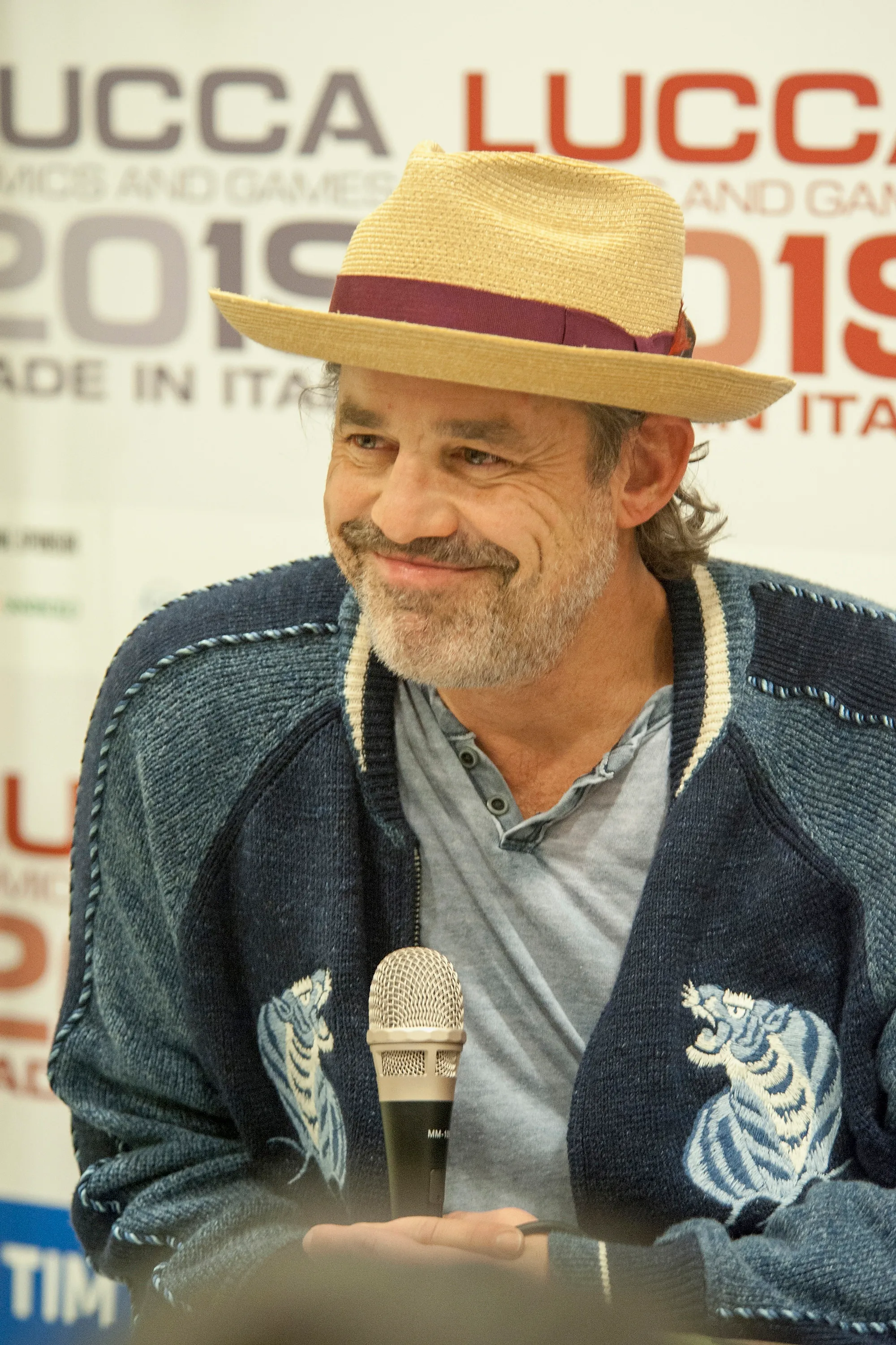 Actor Nicholas Brendon smiling and wearing a straw hat, gray shirt, and blue sweater at Lucca Comics & Games.