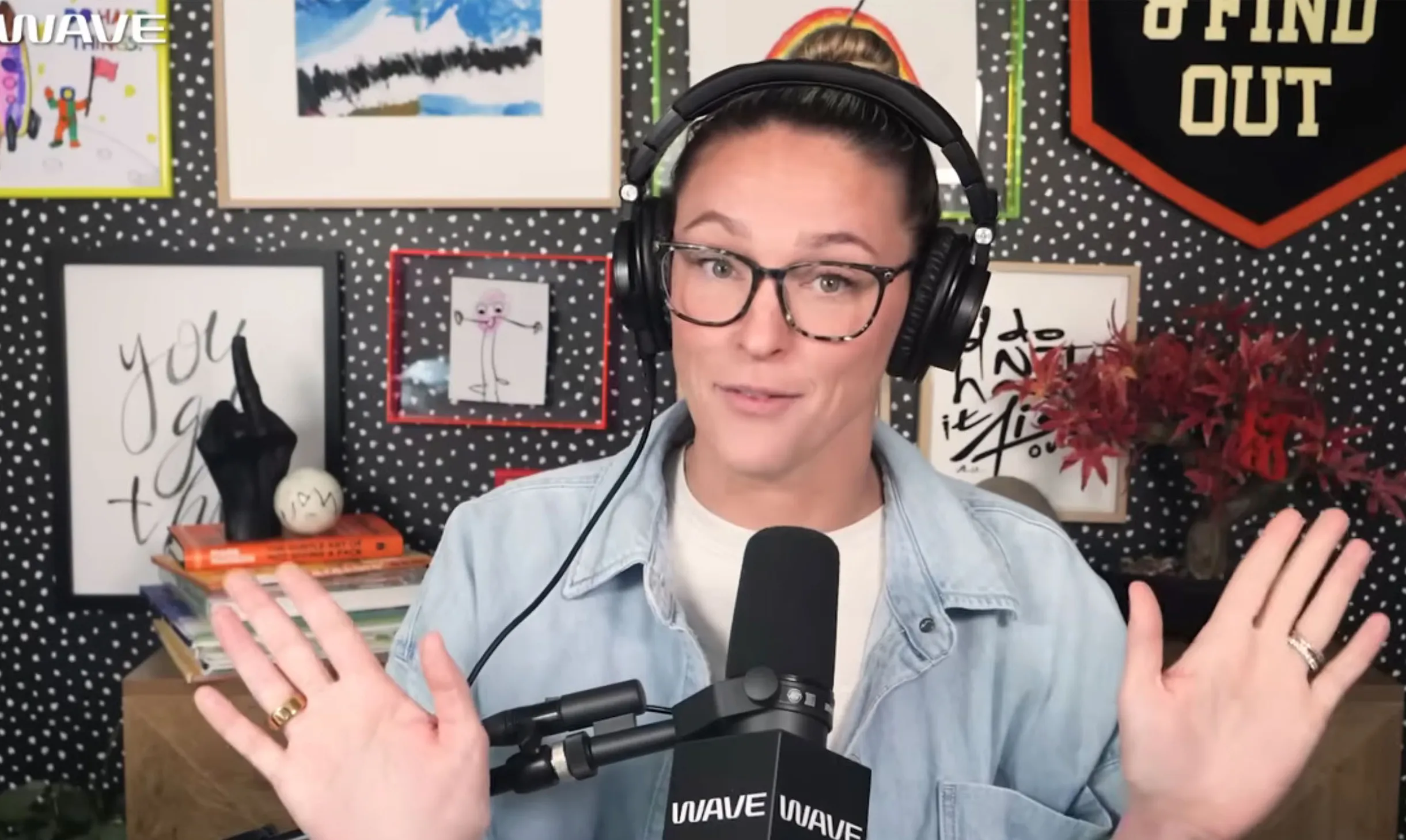 Kylie Kelce, wearing headphones and glasses, speaks into a microphone, gesturing with her hands.