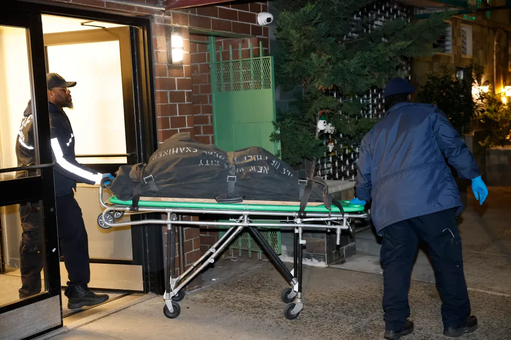 victim in a body bag on a green stretcher being carried out