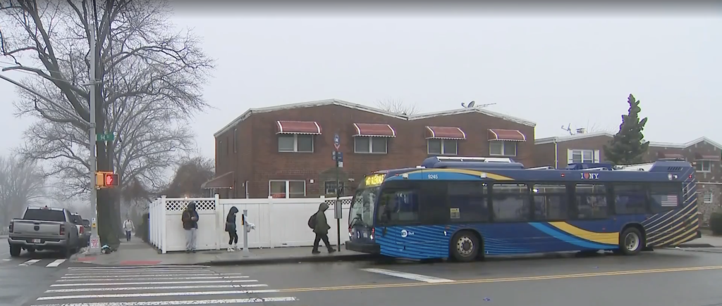 People waiting at a bus stop next to an MTA bus on a misty day.