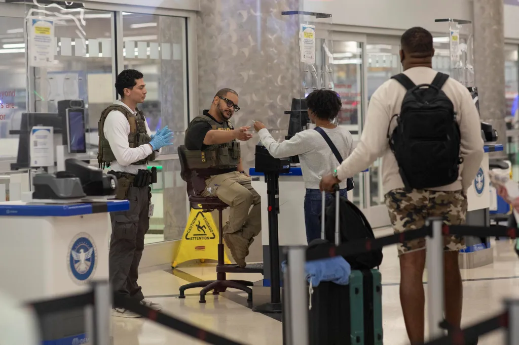 ICE officers checking a passenger's ID at an airport security checkpoint.