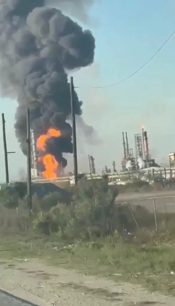 An oil refinery with a large fire and thick black smoke rising into the sky.