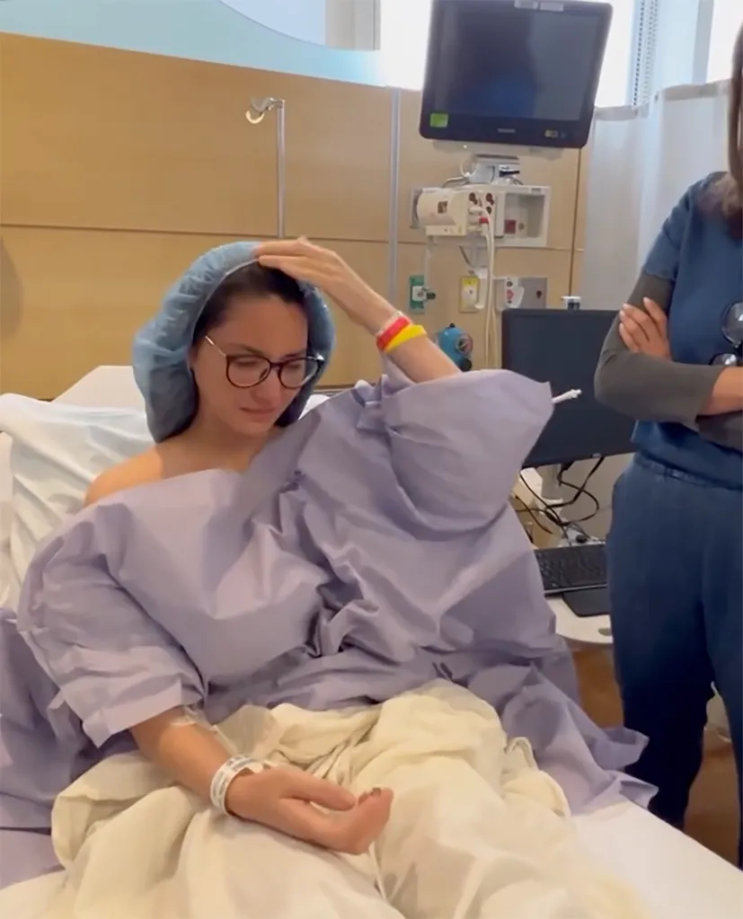 Olivia Munn wearing a medical cap and gown, sitting in a hospital bed with a doctor standing nearby.