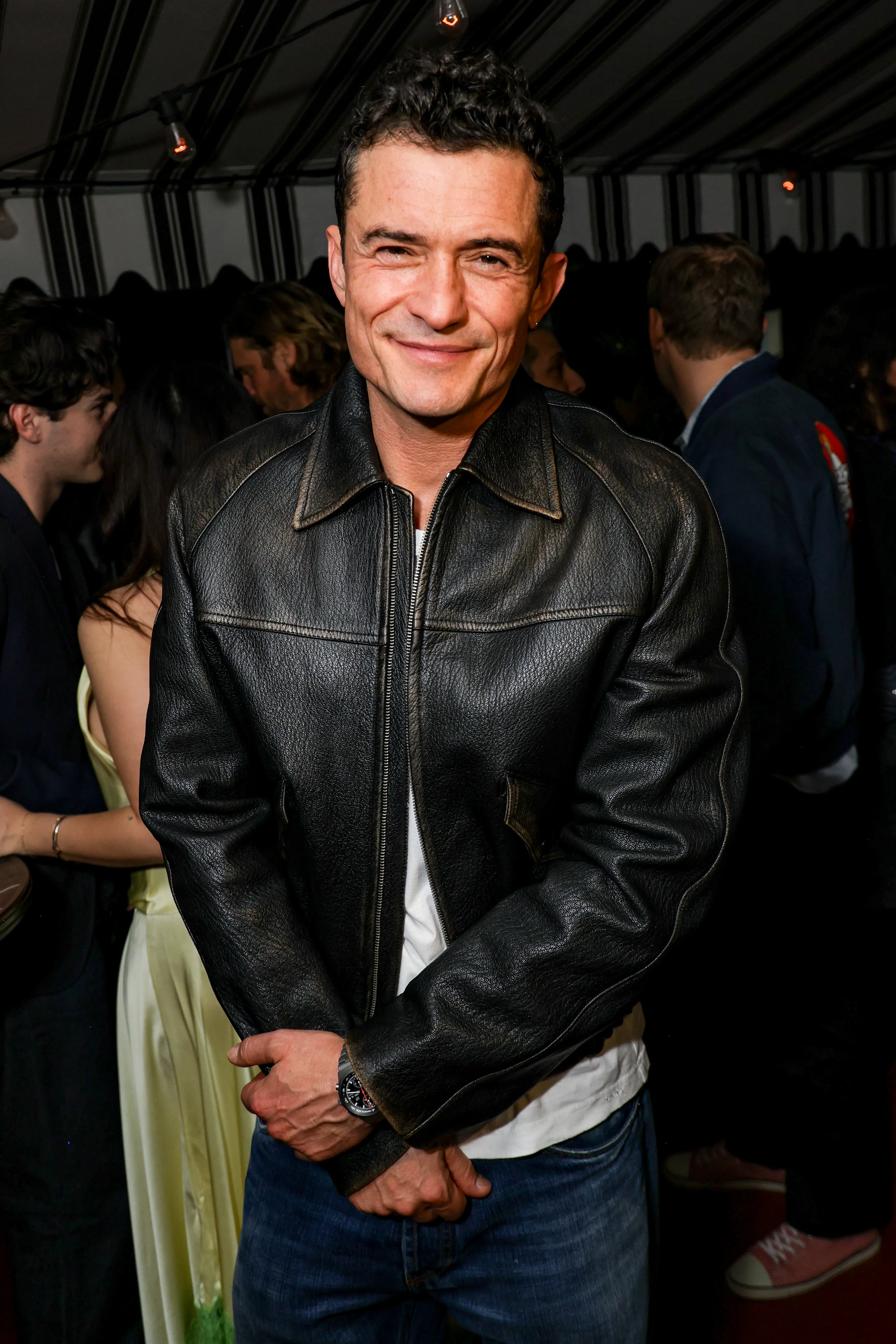 Orlando Bloom in a black leather jacket and jeans, smiling at the Frieze + STAUD Celebrate Frieze Los Angeles 2026 event.