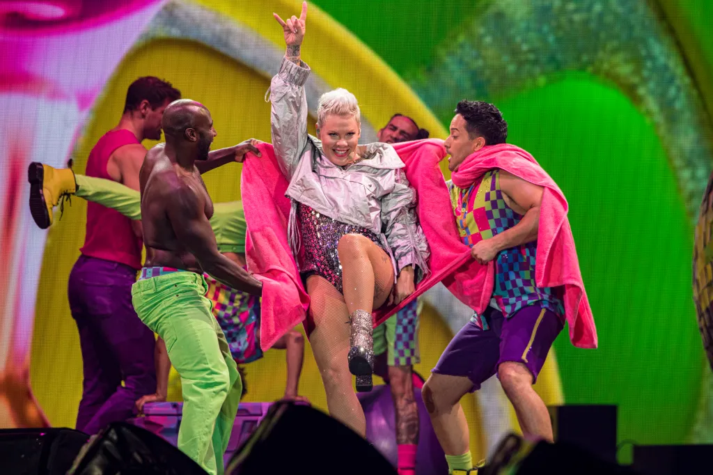 P!nk performing on stage at Petco Park, being held by dancers, with one arm raised in a rock gesture.