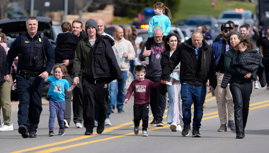 A police officer escorts parents and their children down Walnut Lake Road.