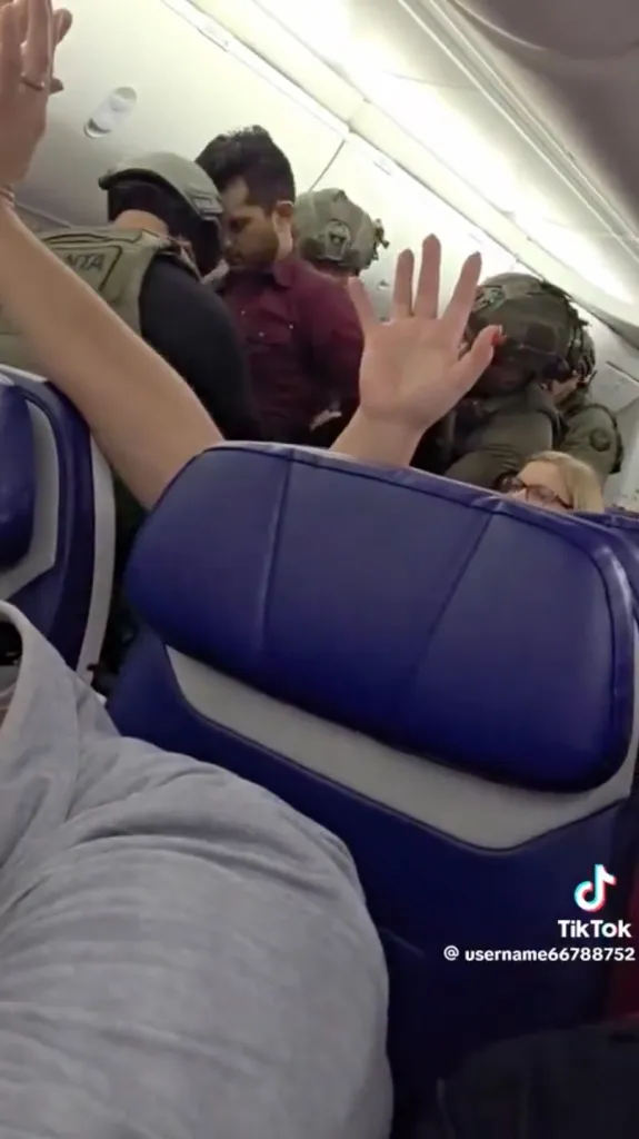 Law enforcement officers detaining a male passenger on an airplane.