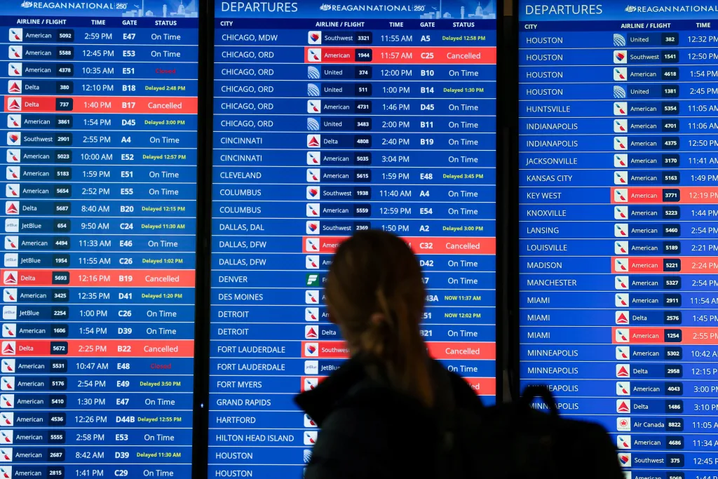 A person looking at a flight departure board at Ronald Reagan Washington National Airport, with several flights listed as cancelled or delayed.