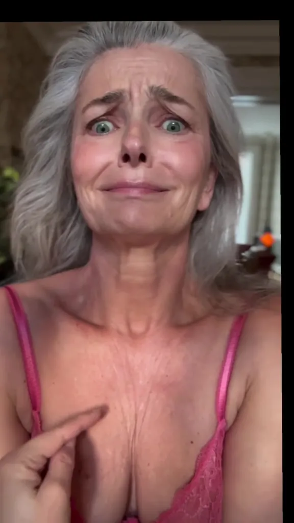Paulina Porizkova in pink lingerie, making a surprised face and pointing at wrinkles on her chest.