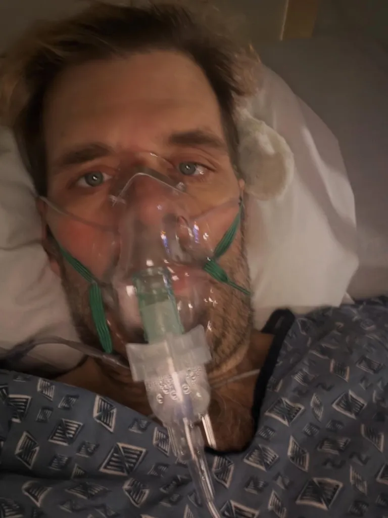 Perez Hilton lying in a hospital bed with an oxygen mask.
