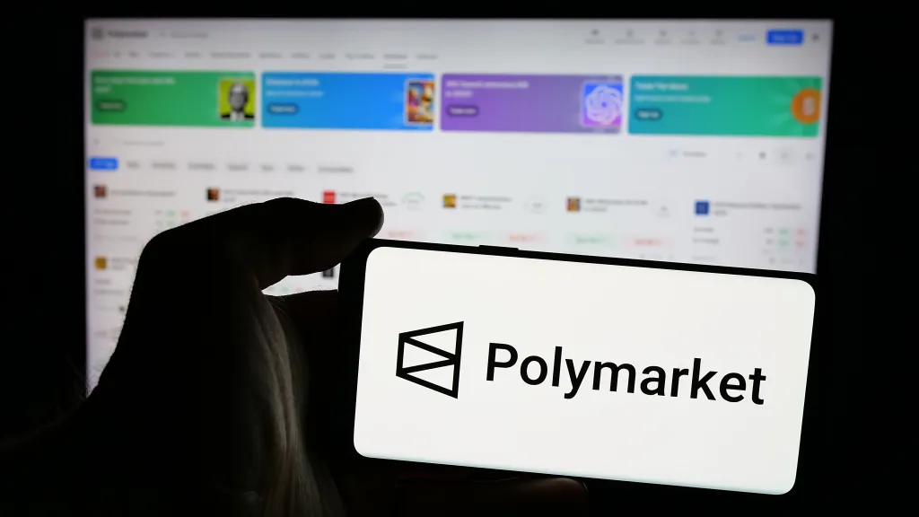 A hand holding a mobile phone displaying the Polymarket logo and name.