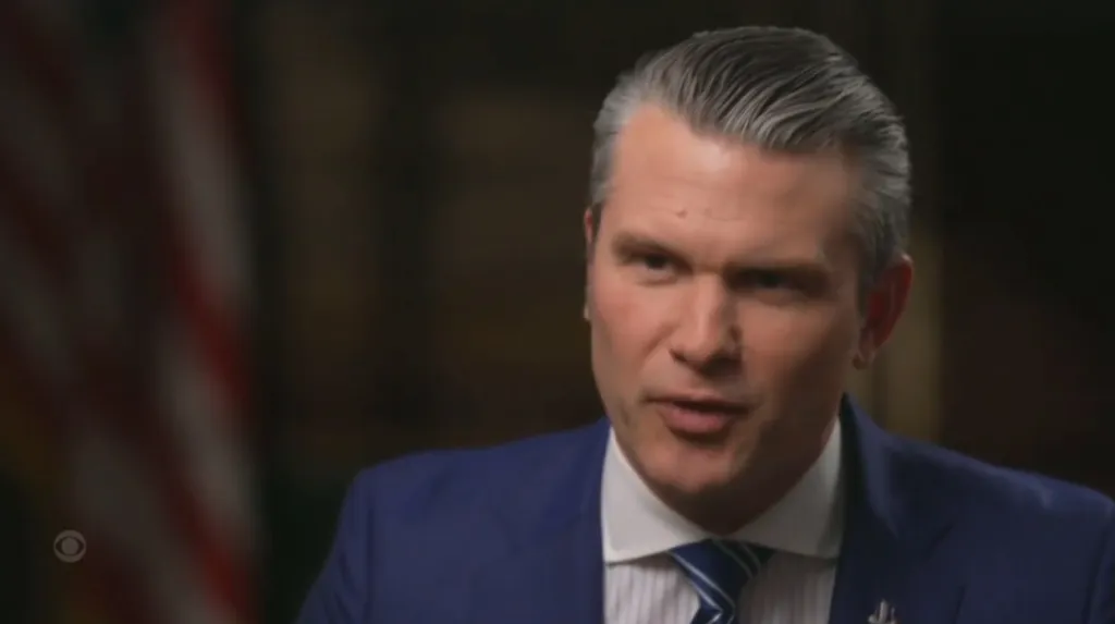 Pete Hegseth speaking, with an American flag faintly visible in the background.