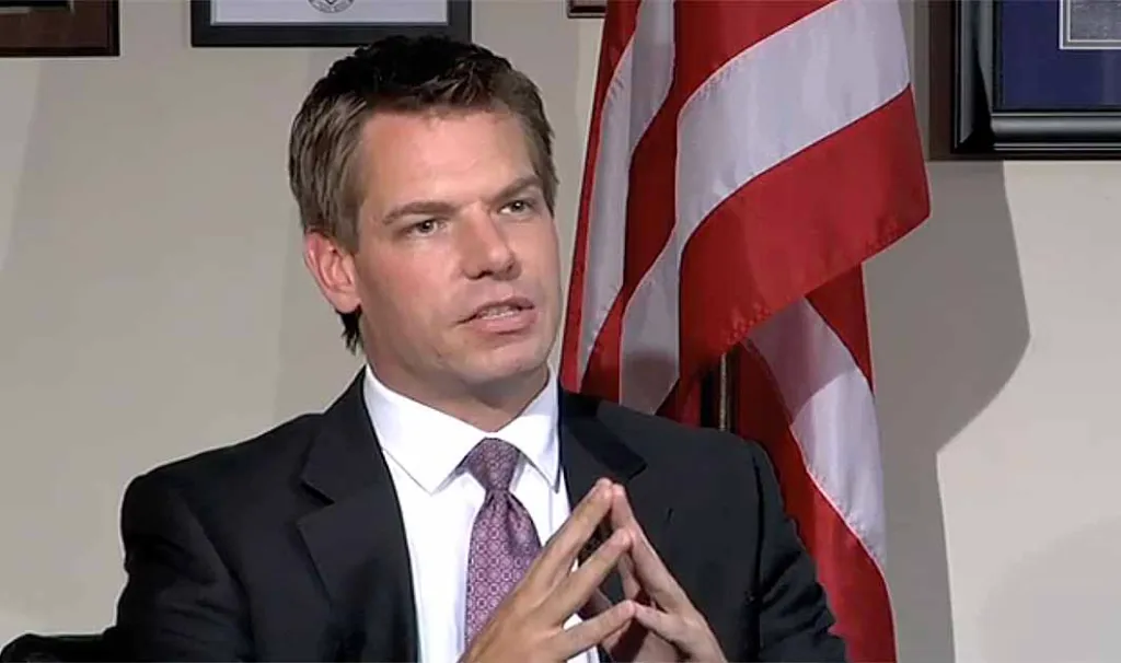 Eric Swalwell speaking with an American flag in the background.