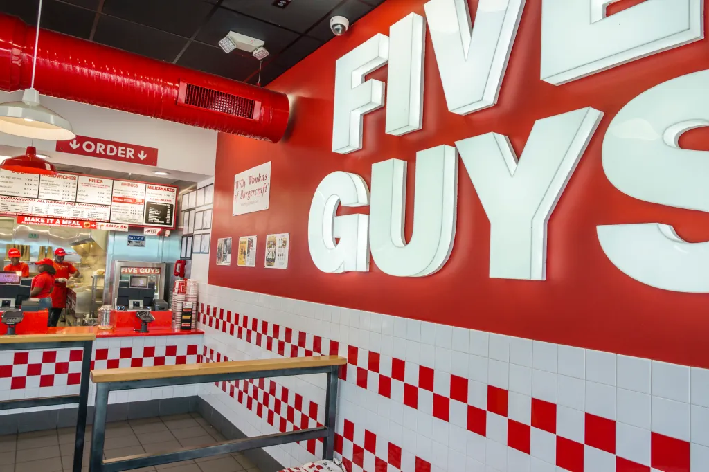 Interior of a Five Guys restaurant with staff behind the counter, menu boards, and the 