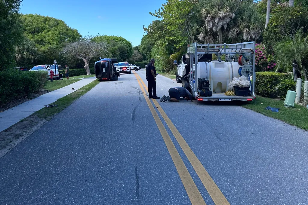 Skid marks on the road next to an overturned vehicle, a white pickup truck, and two police cars at the scene of Tiger Woods' rollover crash in Jupiter Island, Florida.