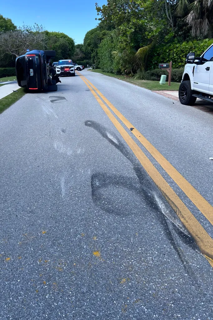 Skid marks and an overturned vehicle from the Tiger Woods crash on a road lined with trees.